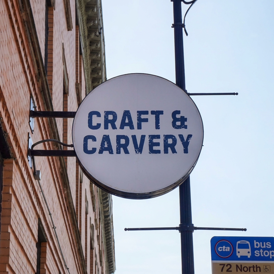 Craft & Carvery restaurant sign mounted on a brick building beside a Chicago CTA bus stop.